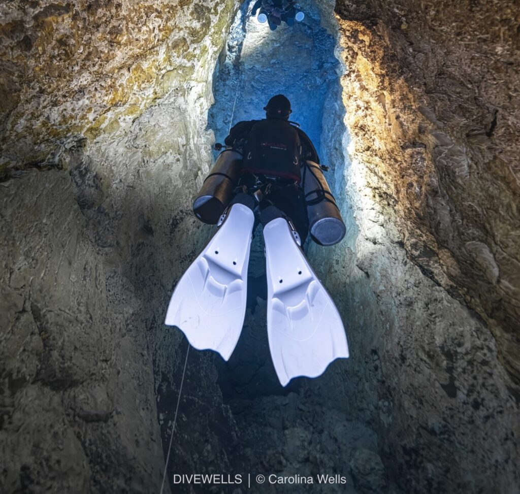 divers swimming through a cave wearing light blue scuba fins