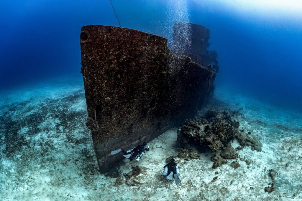 scuba divers exploring a sunken ship in the ocean